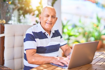 Wall Mural - senior handsome man smiling happy and confident. sitting using laptop at terrace