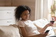 © fizkes - Satisfied young african american woman relaxing on sofa, holding smartphone.