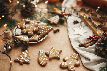 Wall Mural - Christmas gingerbread cookies on vintage plate and anise, cinnamon, pine cones, cedar branches  with golden lights on rustic table. Baked traditional gingerbread man, tree, star cookies