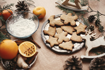 Wall Mural - Christmas gingerbread cookies on vintage plate and anise, ginger, cinnamon, pine cones, fir branches, flour, oranges on rustic table. Baking traditional gingerbread cookies