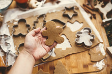 Making christmas gingerbread cookies. Hand holding raw gingerbread man cookie on background of dough, metal cutters and anise, ginger, cinnamon, pine cones, fir branches on rustic table.