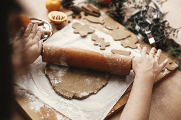 Wall Mural - Making christmas gingerbread cookies. Hands rolling raw dough with wooden rolling pin on background of metal cutters, anise, ginger, cinnamon, pine cones, fir branches on rustic table.