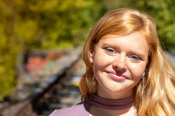 Portrait of gorgeous smiling teenage girl with red hair outdoors on sunny fall day.