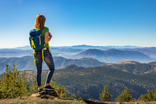 Rear view of female hiker with backpack standing on top of the mountain and enjoying the view during the day.