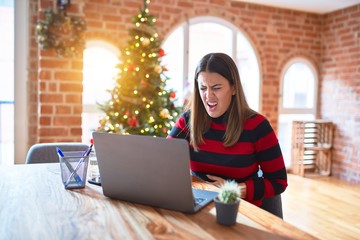 Poster - Beautiful woman sitting at the table working with laptop at home around christmas tree with hand on stomach because nausea, painful disease feeling unwell. Ache concept.