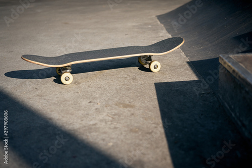 Fotomural View of black skateboard in concrete skatepark on warm day