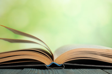 Wall Mural - Open book on blue wooden table against blurred green background, closeup. Space for text