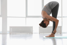 Young Woman Practicing Standing Forward Bend Asana In Yoga Studio. Uttanasana Pose