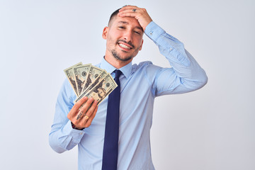 Wall Mural - Young handsome business man holding a bunch of bank notes dollars over isolated background stressed with hand on head, shocked with shame and surprise face, angry and frustrated. Fear and upset 