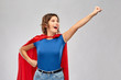 © Syda Productions - women's power and people concept - happy woman in red superhero cape making flying pose over grey background