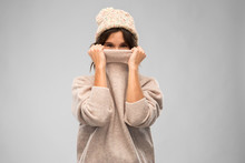 Winter Season And People Concept - Happy Young Woman In Knitted Hat Covering Face With Warm Sweater Over Grey Background