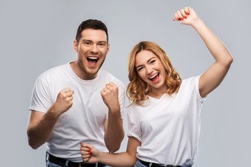 Wall Mural - emotions and people concept - portrait of happy couple in white t-shirts celebrating success over grey background