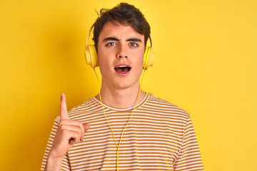 Sticker - Teenager boy wearing headphones over isolated yellow background pointing finger up with successful idea. Exited and happy. Number one.