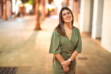 Young beautiful girl smiling happy and confident walking at the town street, standing with a smile on face around night lights bokeh