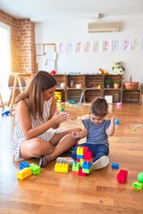 Poster - Young beautiful teacher and toddler playing with building blocks toy at kindergarten