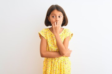 Wall Mural - Young beautiful child girl wearing yellow floral dress standing over isolated white background looking stressed and nervous with hands on mouth biting nails. Anxiety problem.