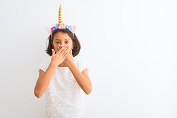 Poster - Beautiful child girl wearing unicorn diadem standing over isolated white background shocked covering mouth with hands for mistake. Secret concept.