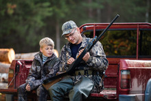 Father And Son Sitting In A Pickup Truck After Hunting In Forest. Dad Showing Boy Mechanism Of A Shotgun Rifle.