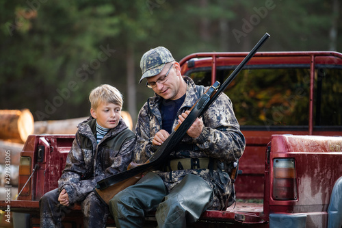 Cuadros en Lienzo Father and son sitting in a pickup truck after hunting in forest