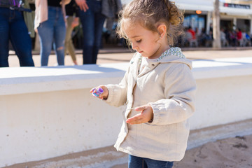 Beautiful toddler child girl wearing jacket playing with the sand on the beach