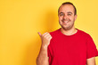 © Krakenimages.com - Young man wearing red casual t-shirt standing over isolated yellow background pointing and showing with thumb up to the side with happy face smiling