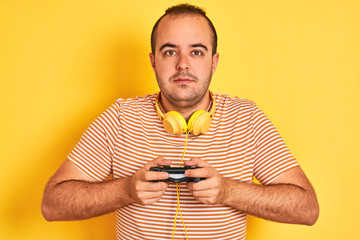 Poster - Young gamer man playing video game using headphones over isolated yellow background with a confident expression on smart face thinking serious