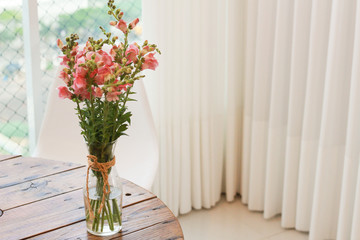 simple snapdragons arrangement on wooden table in a home interior corner, bright and with white curtains 