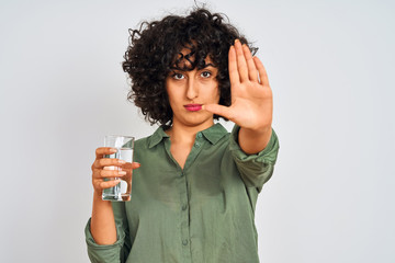 Sticker - Young arab woman with curly hair holding glass of water over isolated white background with open hand doing stop sign with serious and confident expression, defense gesture