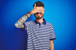 © Krakenimages.com - Young man with tattoo wearing striped polo standing over isolated blue background smiling and laughing with hand on face covering eyes for surprise. Blind concept.