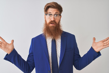 Wall Mural - young redhead irish businessman wearing suit and glasses over isolated white background clueless and