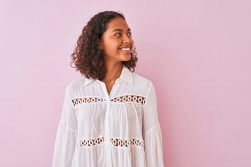 young brazilian woman wearing shirt standing over isolated pink background smiling looking side and 