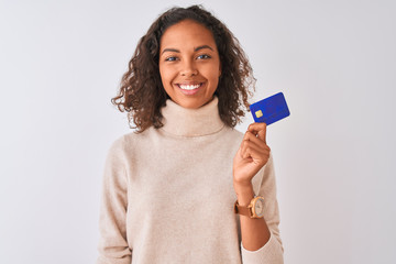 Poster - Young brazilian woman holding credit card standing over isolated white background with a happy face standing and smiling with a confident smile showing teeth