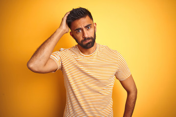 Wall Mural - Young indian man wearing t-shirt standing over isolated yellow background worried and stressed about a problem with hand on forehead, nervous and anxious for crisis