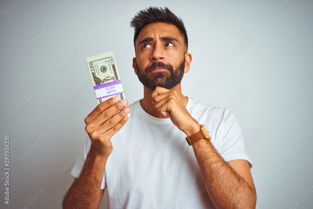 Young indian man holding dollars standing over isolated white ...