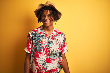 Wall Mural - Afro american man with dreadlocks wearing floral shirt and hat over isolated yellow background looking away to side with smile on face, natural expression. Laughing confident.