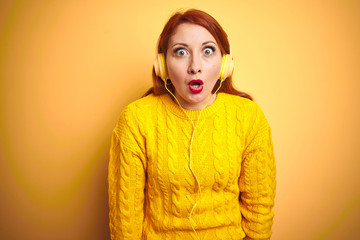 Sticker - Young redhead woman listening to music using headphones over yellow isolated background afraid and shocked with surprise expression, fear and excited face.