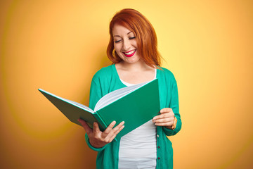 Wall Mural - Young redhead student woman reading green book over yellow isolated background with a happy face standing and smiling with a confident smile showing teeth