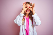 Young Beautiful Doctor Woman Using Stethoscope Over Pink Isolated Background Doing Ok Gesture Like Binoculars Sticking Tongue Out, Eyes Looking Through Fingers. Crazy Expression.