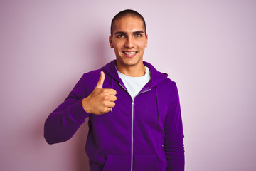 Poster - Young handsome man wearing purple sweatshirt over pink isolated background doing happy thumbs up gesture with hand. Approving expression looking at the camera with showing success.