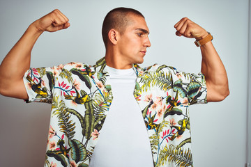 Poster - Young handsome man on holidays wearing Hawaiian shirt over white background showing arms muscles smiling proud. Fitness concept.