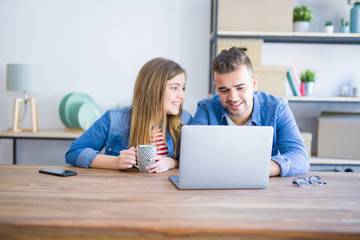 Poster - Young couple relaxing drinking a coffee and using the computer laptop around cardboard boxes, very happy moving to a new house