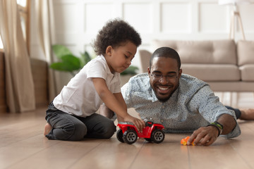 Smiling black dad playing toy cars with little son