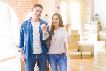 Poster - Beautiful young couple moving to a new house smiling with happy face looking and pointing to the side with thumb up.