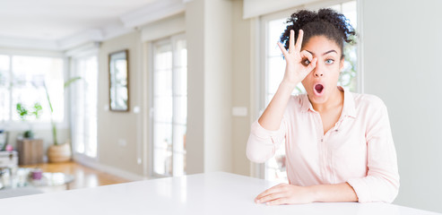 Poster - Wide angle of beautiful african american woman with afro hair doing ok gesture shocked with surprised face, eye looking through fingers. Unbelieving expression.