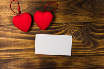 Valentine's day blank greeting card and two red hearts on wooden background