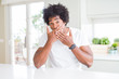 © Krakenimages.com - Young african american man wearing casual white t-shirt sitting at home shocked covering mouth with hands for mistake. Secret concept.