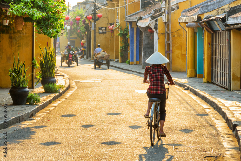 Vietnamese woman in traditional hat bicycling along Hoi An - obrazy, fototapety, plakaty 
