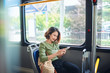 © makistock - Beautiful happy young woman sitting in city bus, looking at mobile phone
