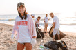 Smiling young girl volunteer cleaning beach from garbage