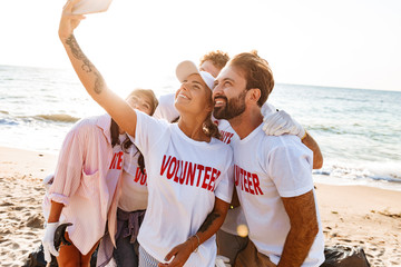 Wall Mural - Image of smiling attractive volunteers taking selfie photo on cellphone